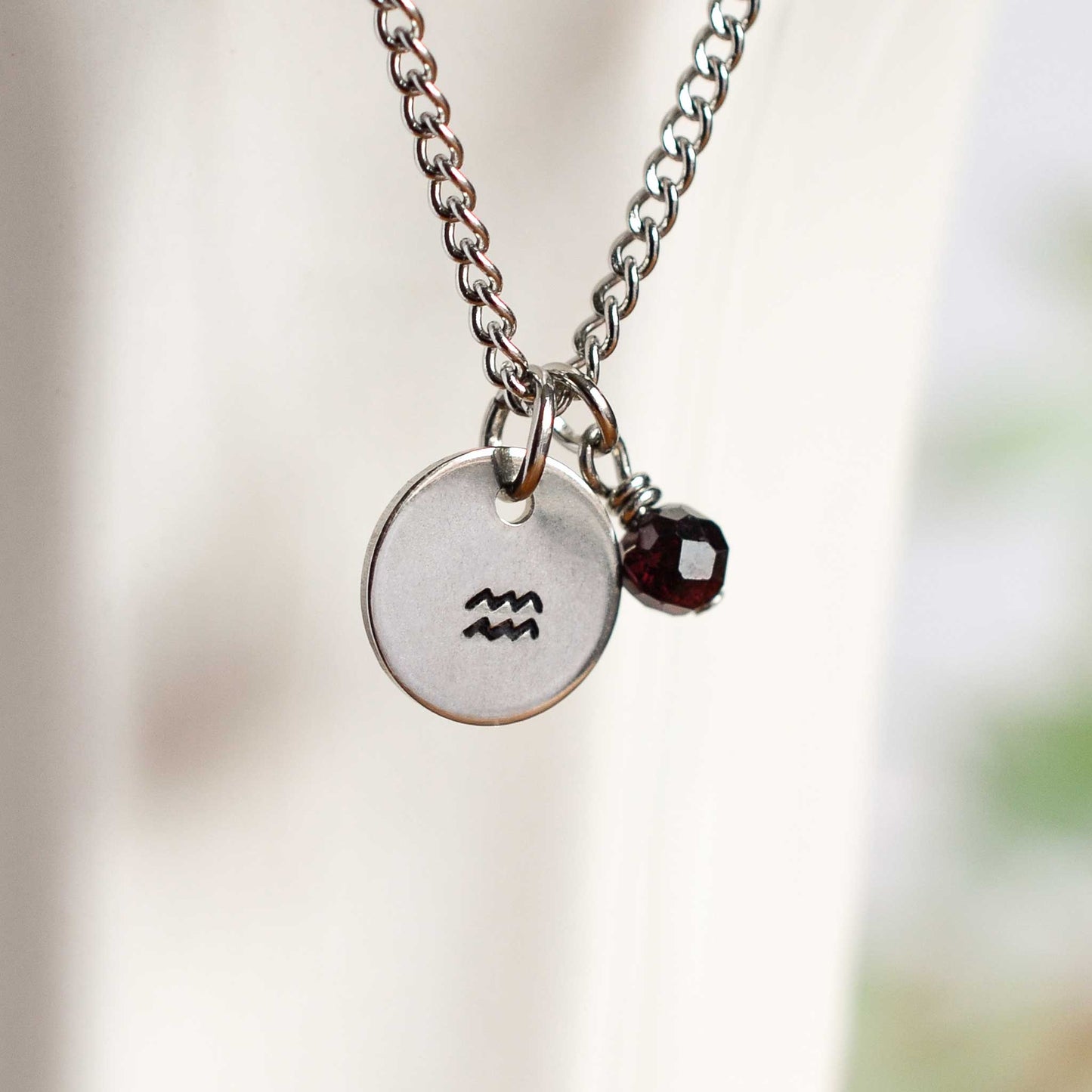 Close up of Aquarius zodiac sign necklace with Garnet gemstone charm on stainless steel chain