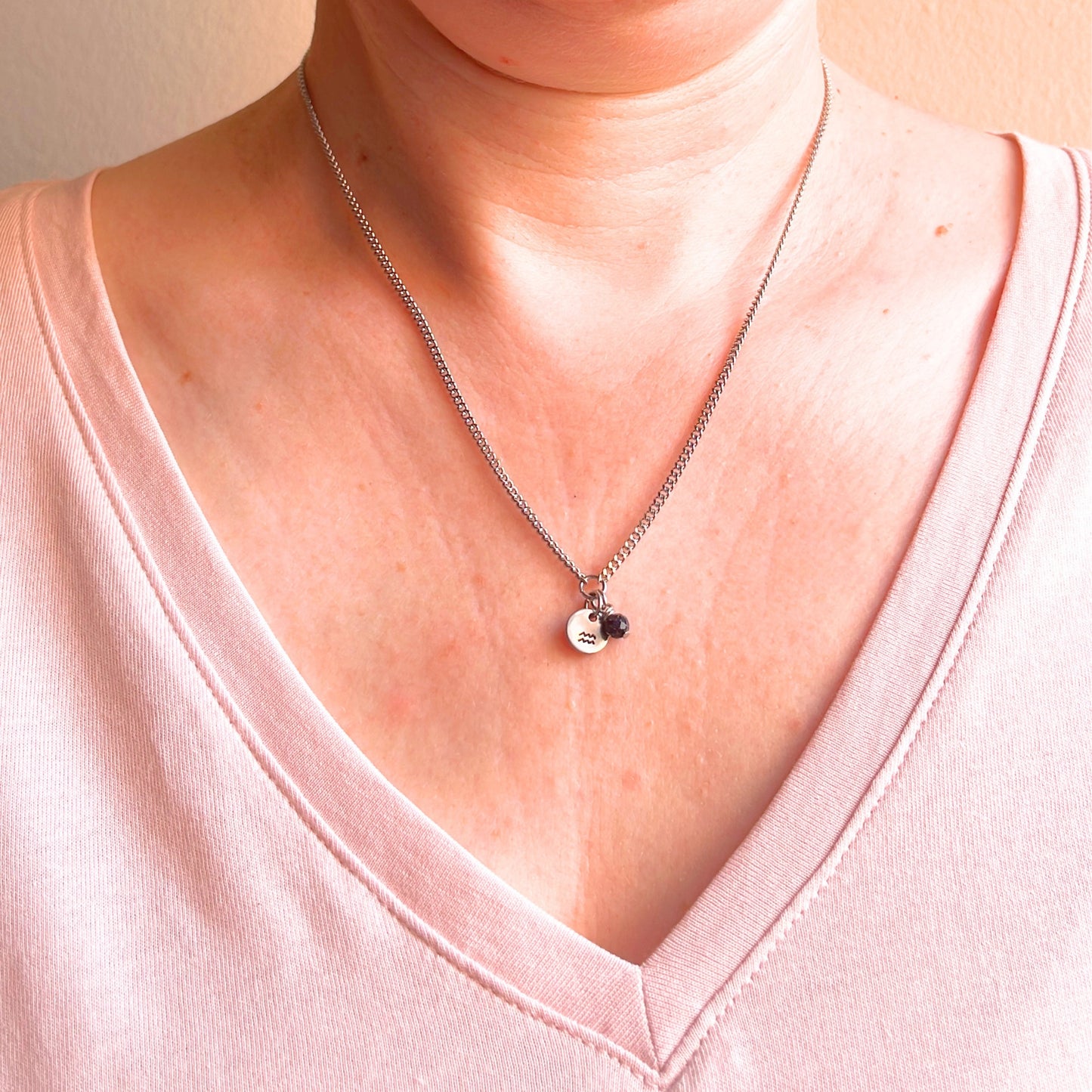 Woman wearing a pink v neck top and dainty Aquarius zodiac sign necklace.