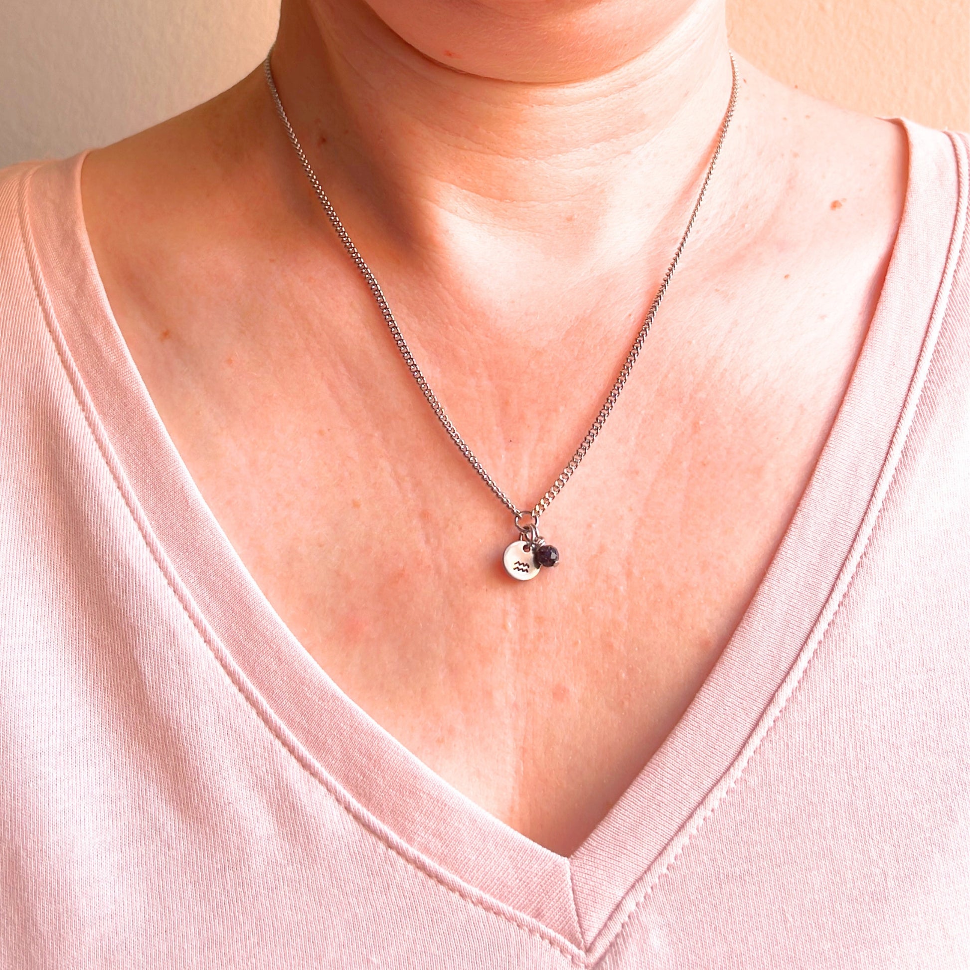 Woman wearing a pink v neck top and dainty Aquarius zodiac sign necklace.