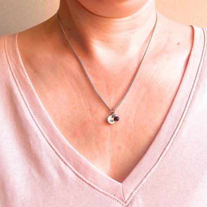 Woman wearing a pink v neck top and dainty Aquarius zodiac sign necklace.
