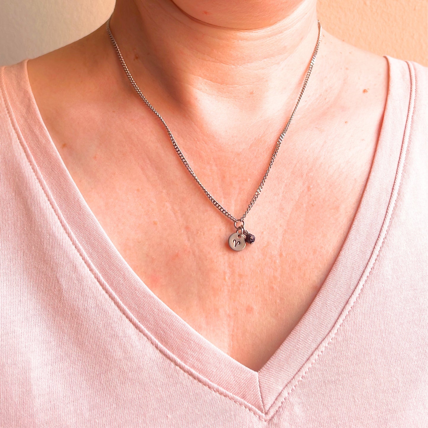 Woman wearing a pink v neck top and dainty Aries zodiac sign necklace.