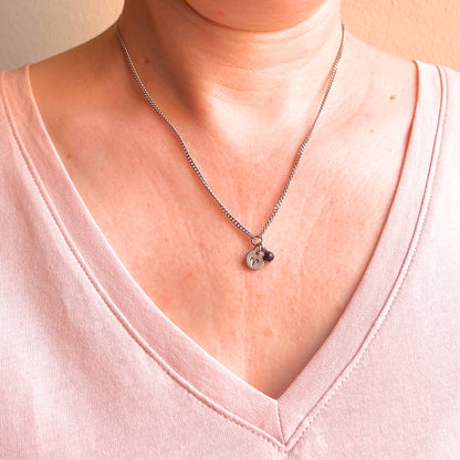 Woman wearing a pink v neck top and dainty Aries zodiac sign necklace.