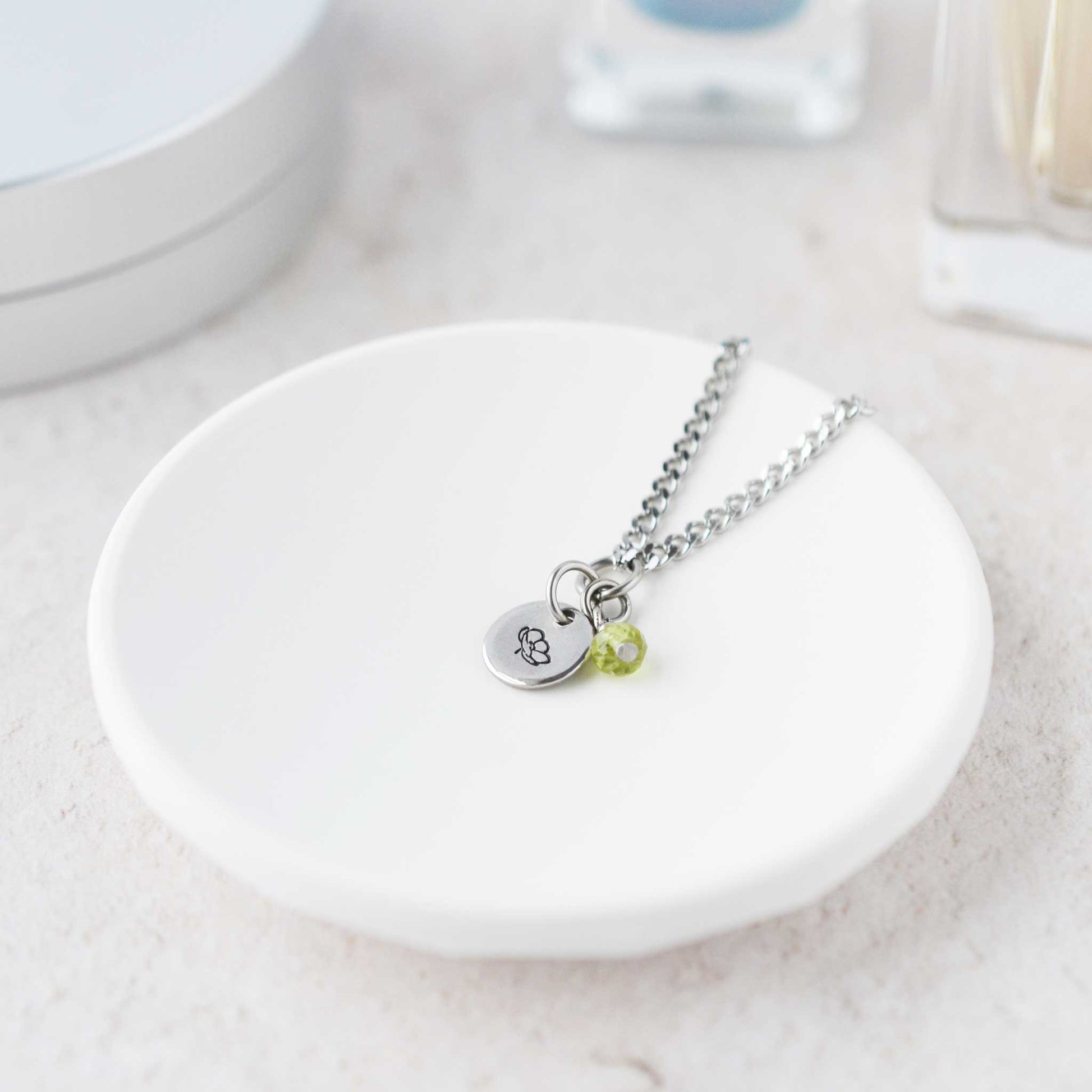 Tiny Poppy & Peridot gemstone necklace laying in white trinket dish