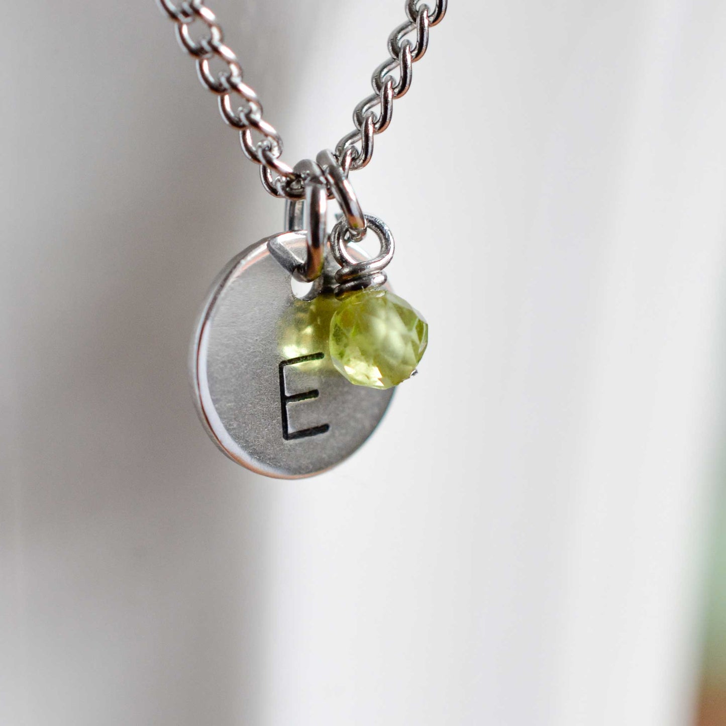 Close up of letter E disc initial pendant with Peridot August birthstone charm