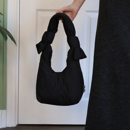 Black handbag with a bow held by a hand against a white door.