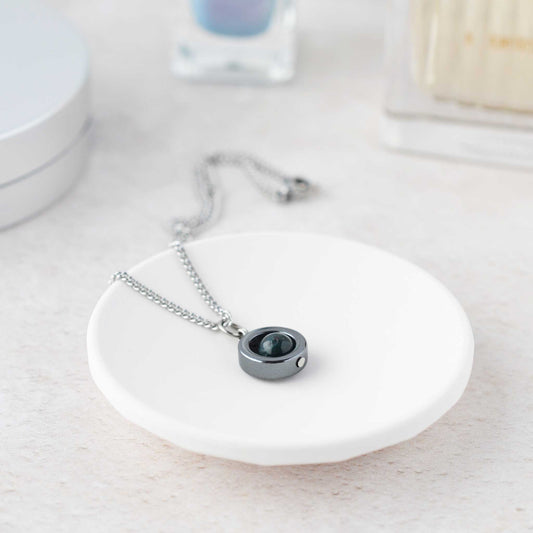 Bloodstone gemstone spinner necklace laying on white trinket dish.