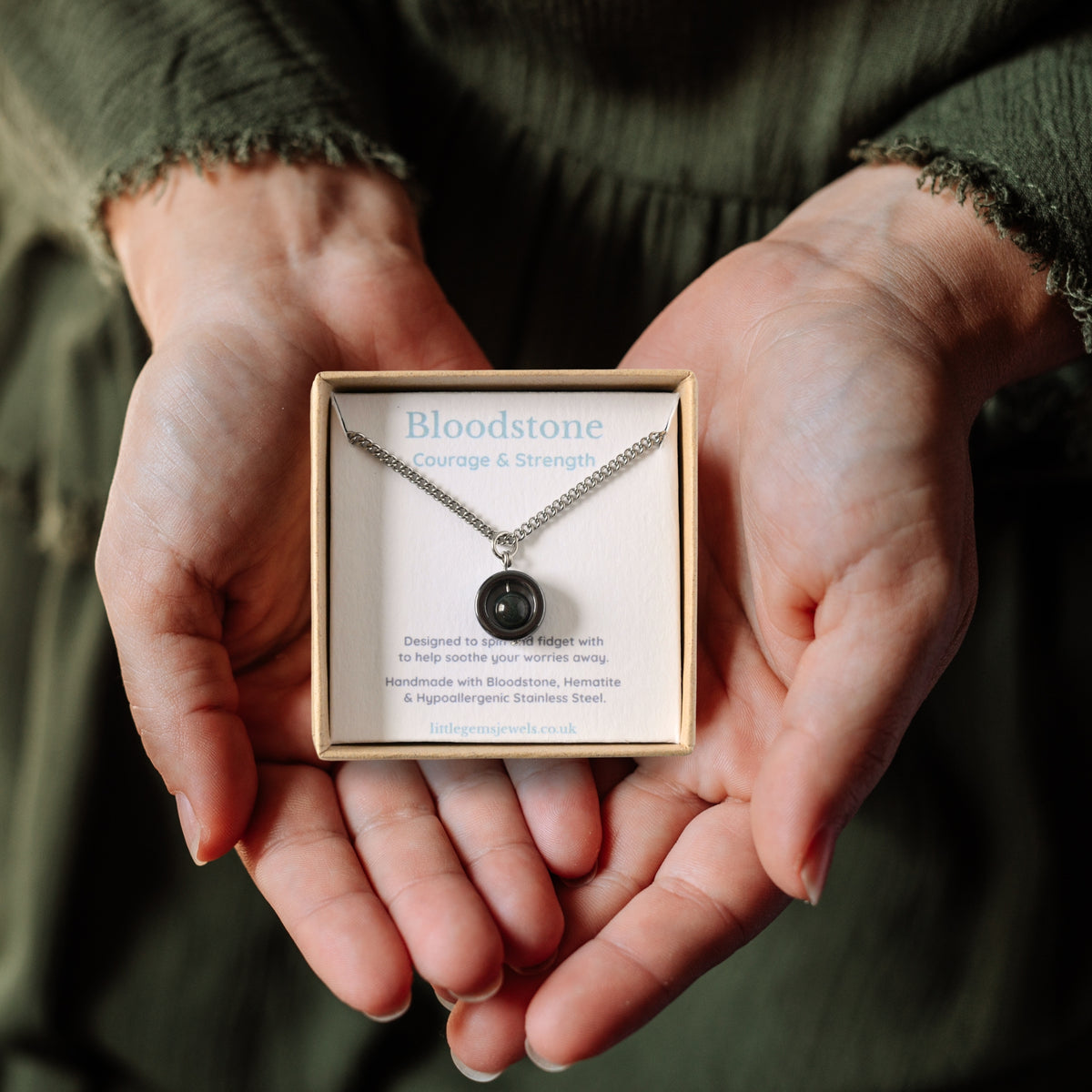 Bloodstone gemstone spinner necklace in a gift box being held in a woman's hands.