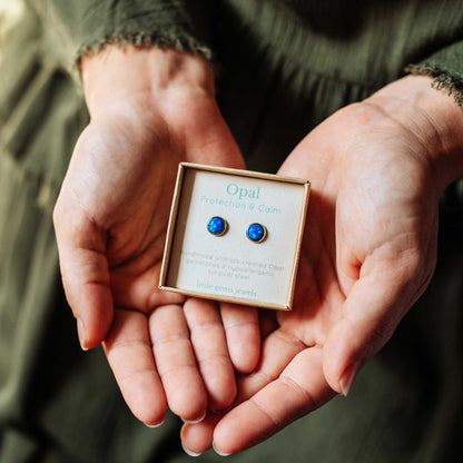 Opal earrings in a box held in hands against a blurred background