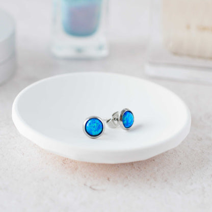 Blue opal stud earrings on a white dish with a blurred background