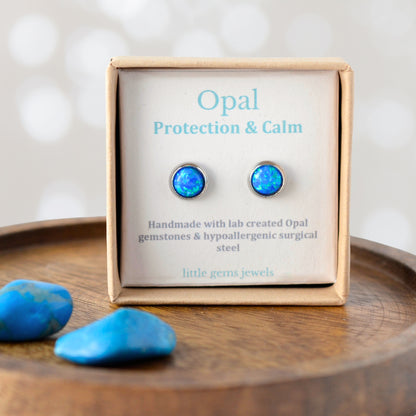 Opal earrings in a 'Protection & Calm' box on a wooden surface with blue stones.