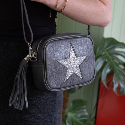 Grey crossbody bag with a star design held by a person, with a blurred indoor background.