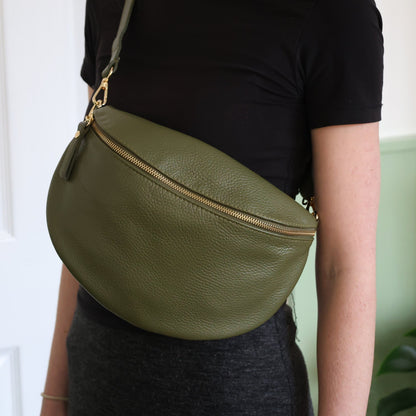 Person wearing a green leather bag over their shoulder against a white wall.