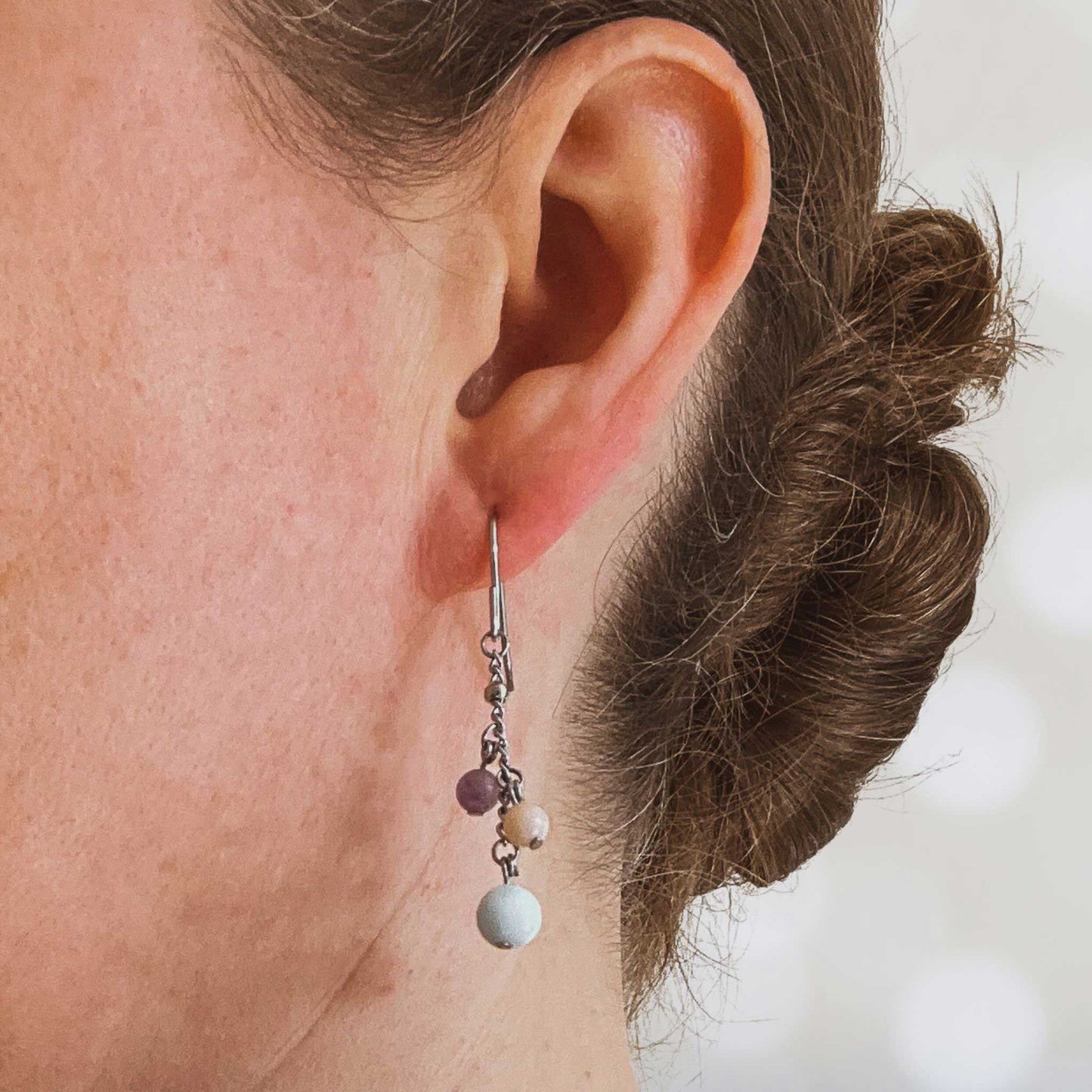 Women wearing blue, pink & purple gemstone drop earring in earlobe