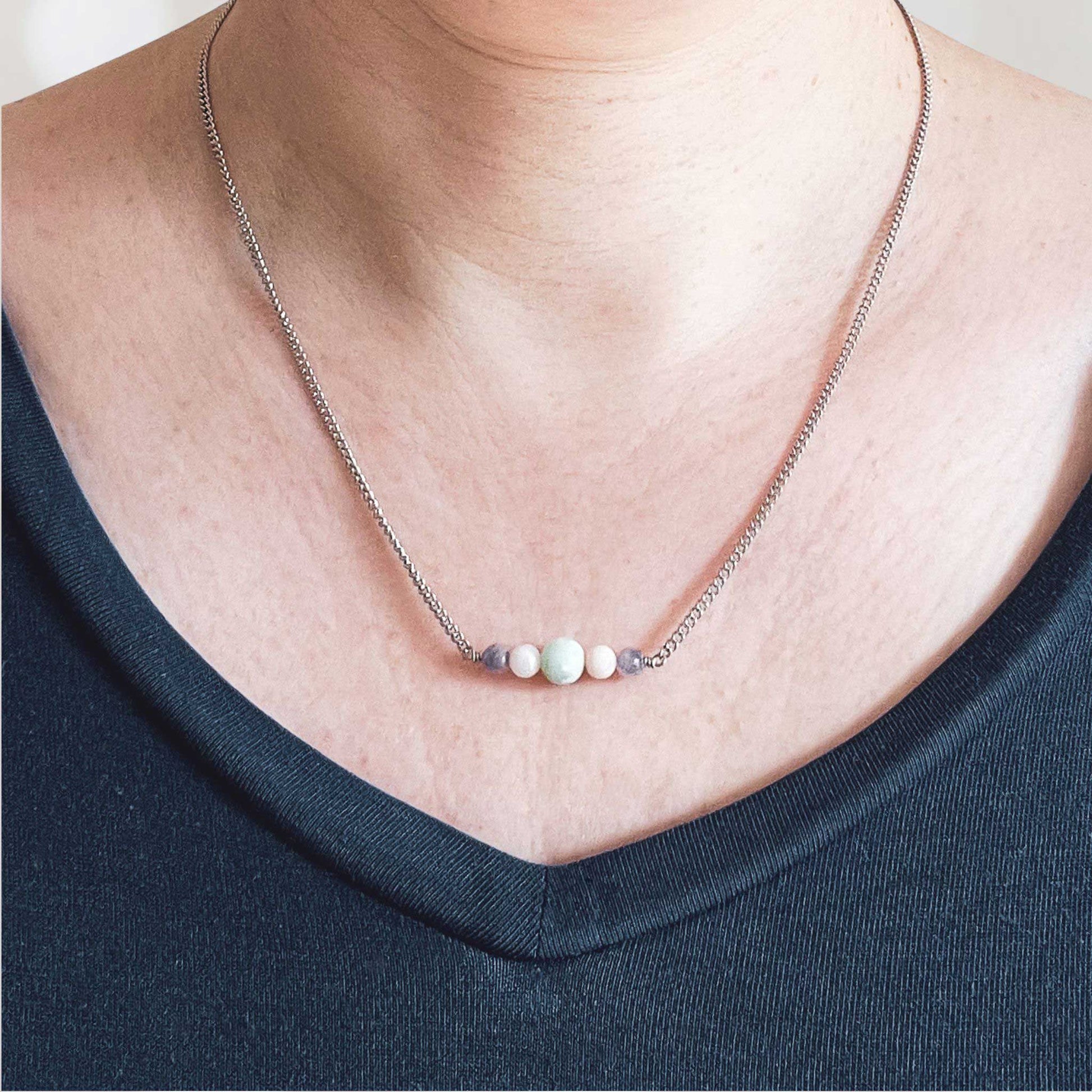Woman wearing dark blue v neck top and dainty pastel gemstone necklace