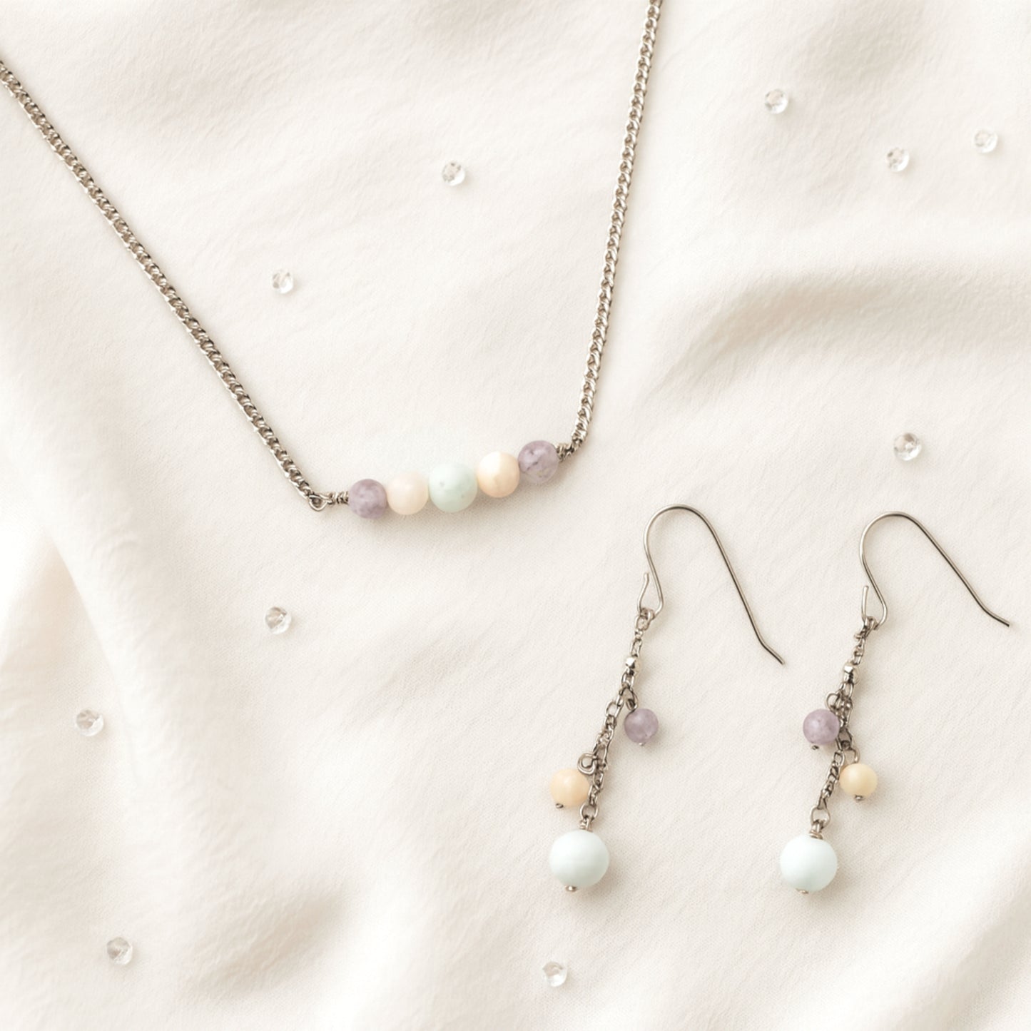 Pastel gemstone bead necklace and earrings on beige fabric.