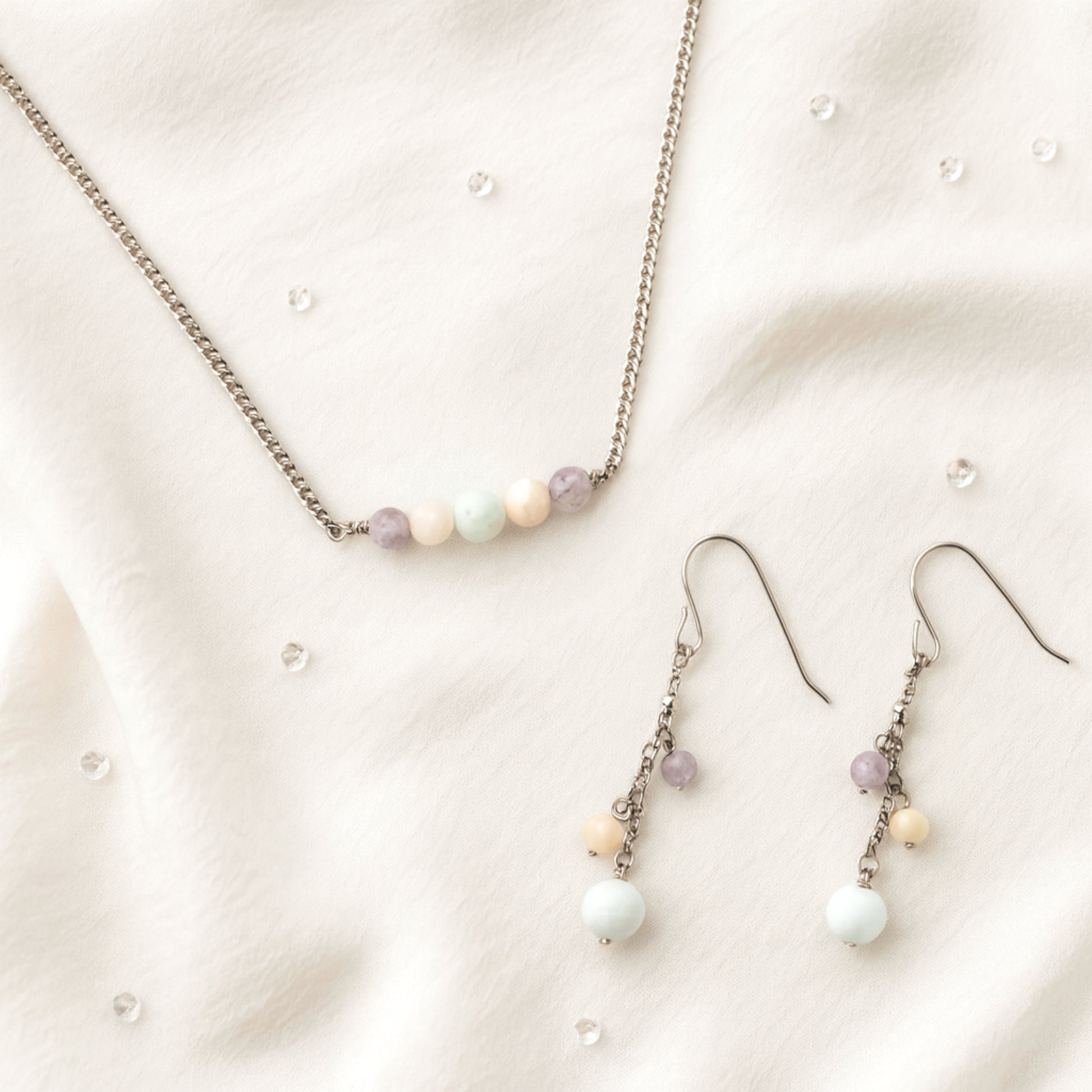 Pastel gemstone bead necklace and earrings on beige fabric.