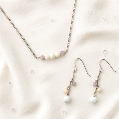 Pastel gemstone bead necklace and earrings on beige fabric.