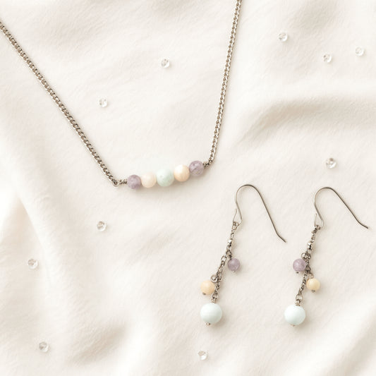 Pastel gemstone bead necklace and earrings on beige fabric.