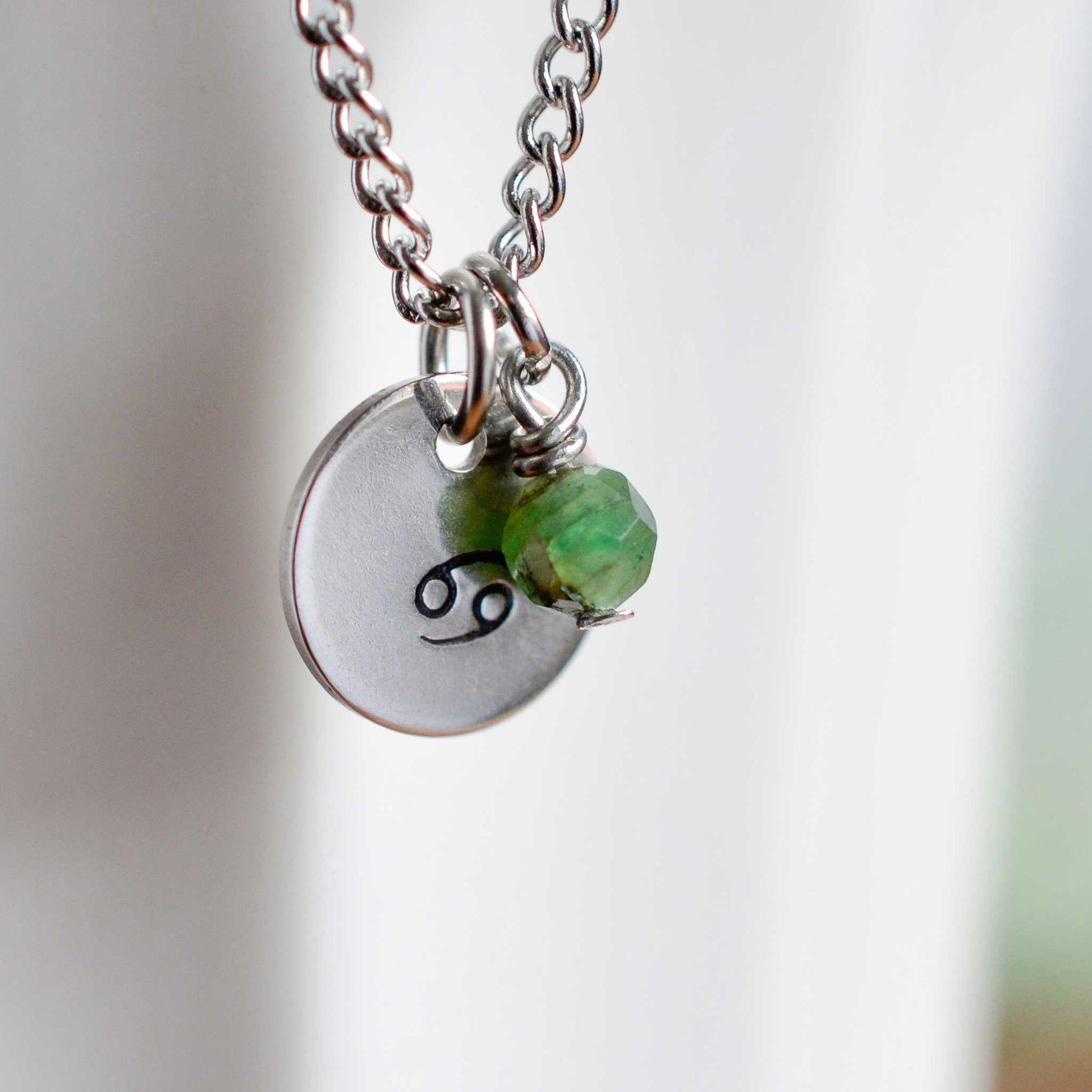 Close up of Cancer zodiac sign necklace with Emerald gemstone charm on stainless steel chain