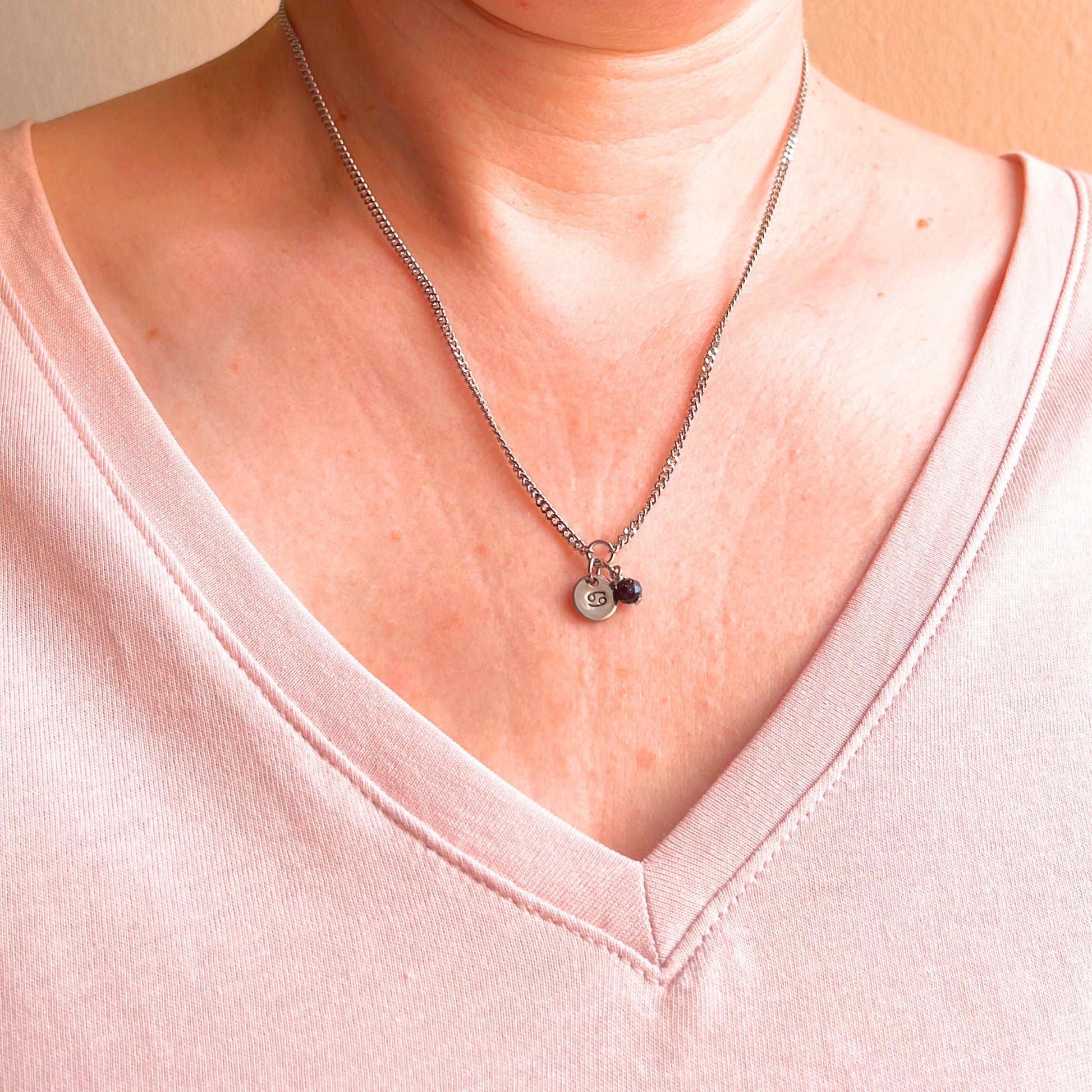 Woman wearing a pink v neck top and dainty Cancer zodiac sign necklace.