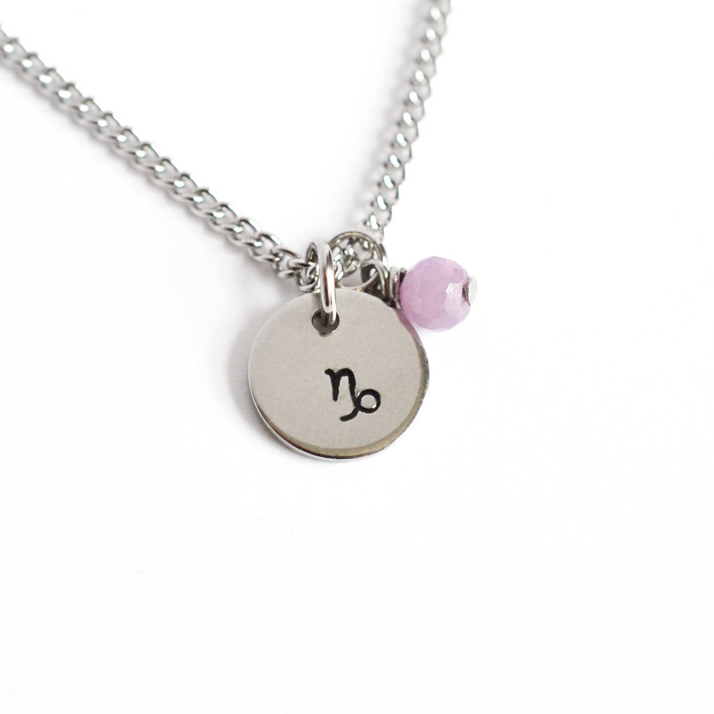 Capricorn Zodiac pendant necklace with tiny Ruby gemstone charm on white background