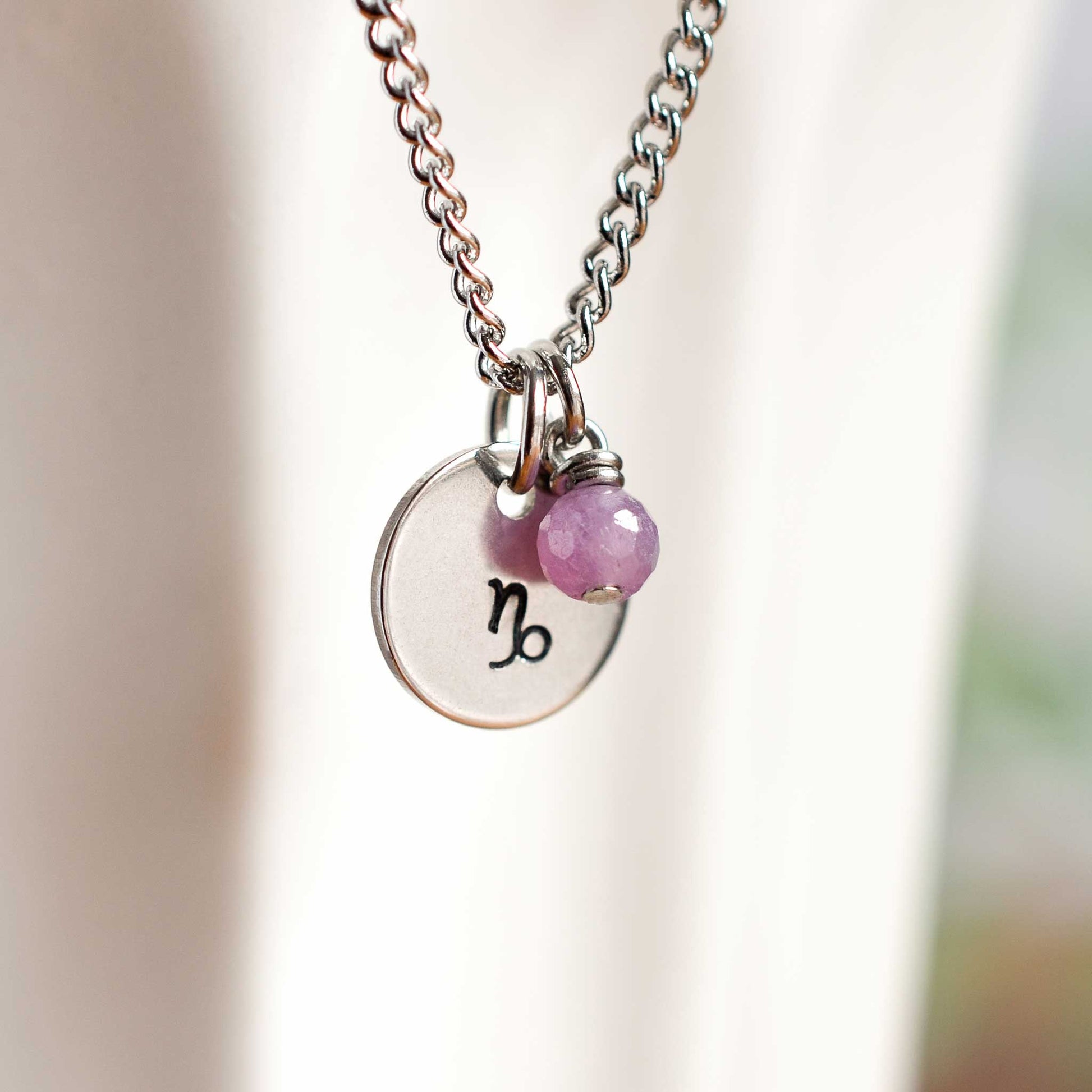 Close up of Capricorn zodiac sign necklace with Ruby gemstone charm on stainless steel chain