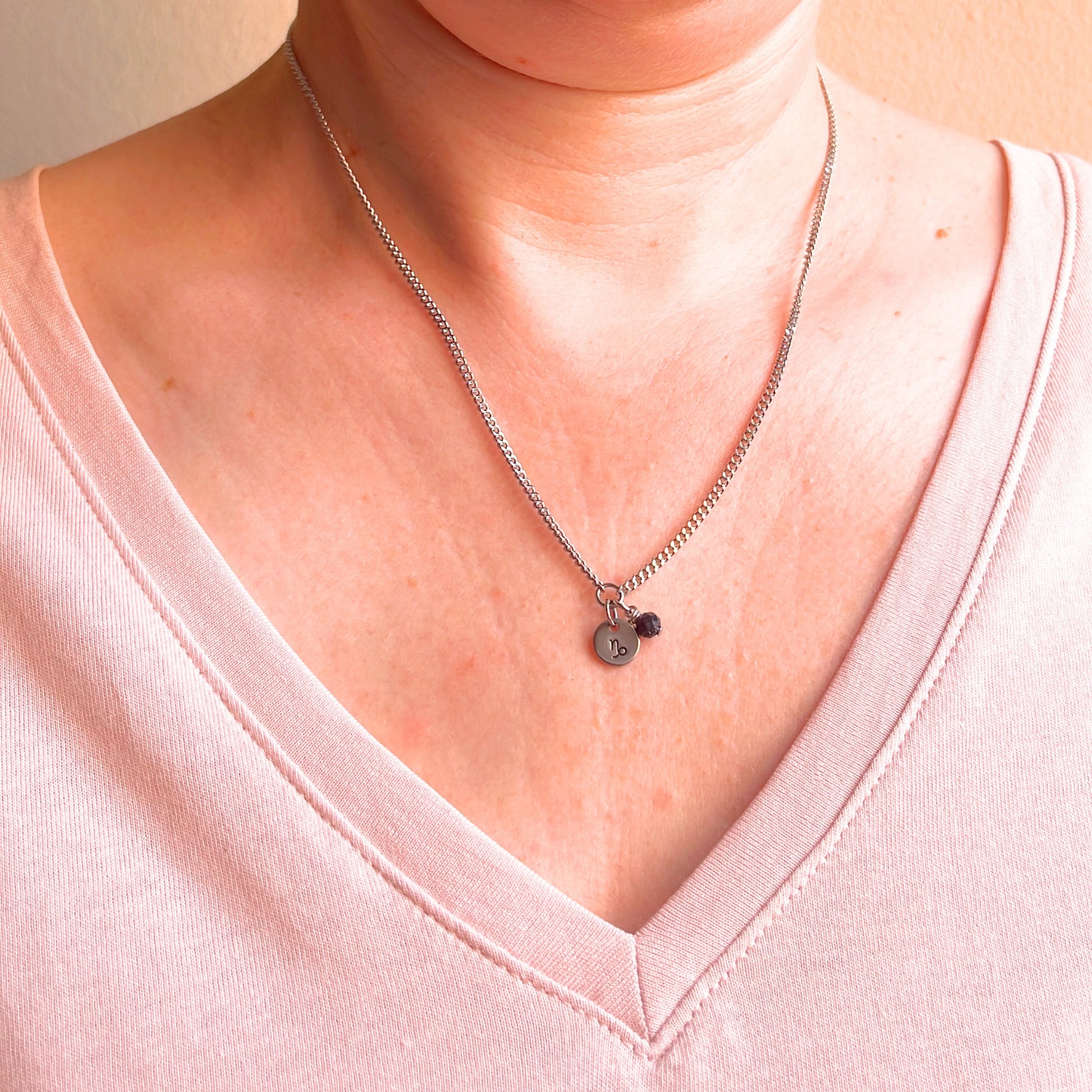 Woman wearing a pink v neck top and dainty Capricorn zodiac sign necklace.