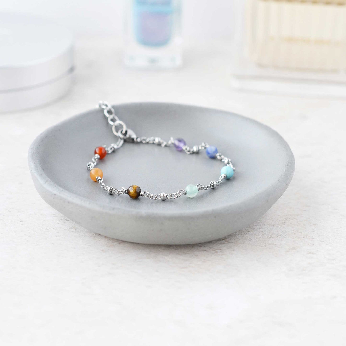 Dainty chakra bracelet in grey trinket dish on dressing table.