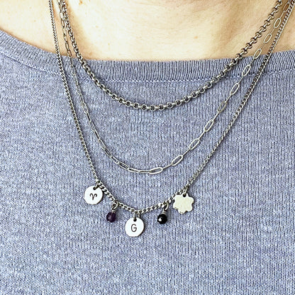 Woman wearing three chains in a layered style with charms hanging on the longest chain.