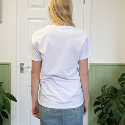 Person wearing a plain white t-shirt in a room with plants and a door.