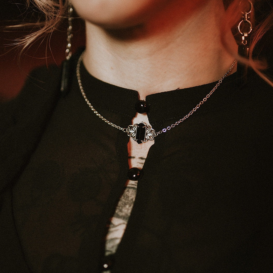 Close-up of a person wearing a black top with a steel necklace featuring a central gemstone.