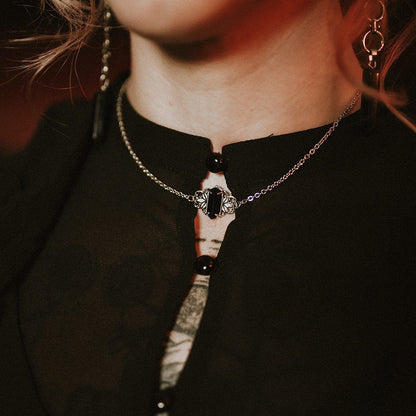 Close-up of a person wearing a black top with a steel necklace featuring a central gemstone.
