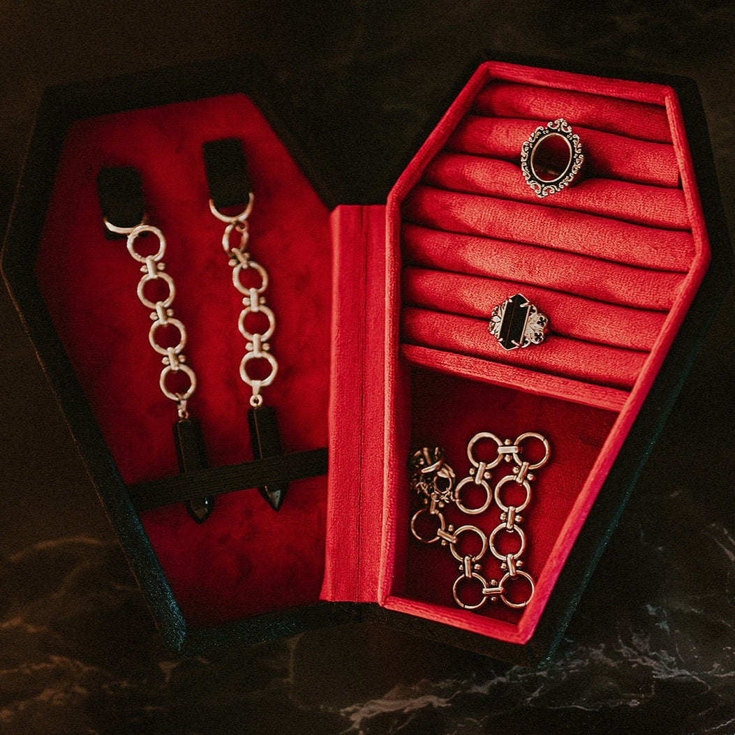 Red jewelry box with black interior containing silver jewelry on a dark background