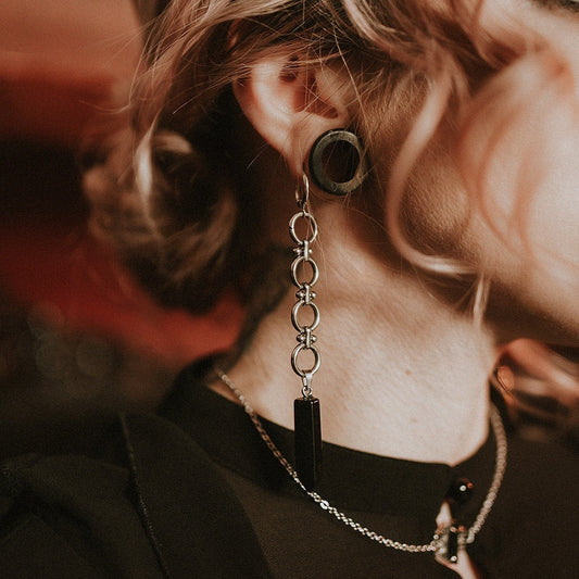 Close-up of a person wearing a unique earring with a chain and black pendant.