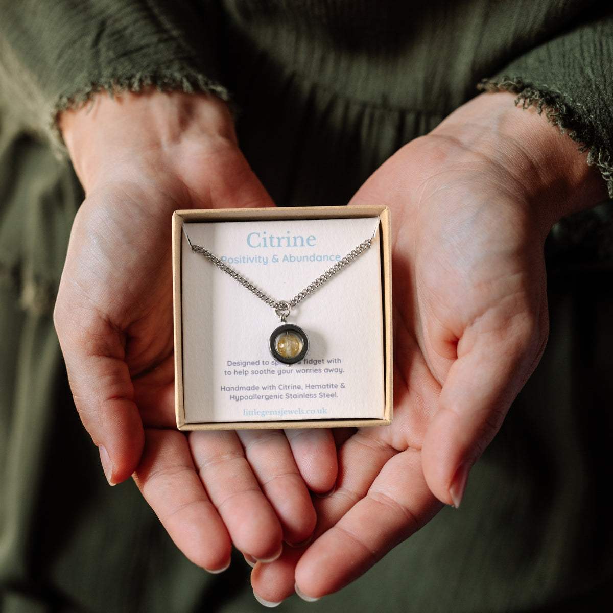 Citrine gemstone spinner necklace in a gift box being held in a woman's hands.