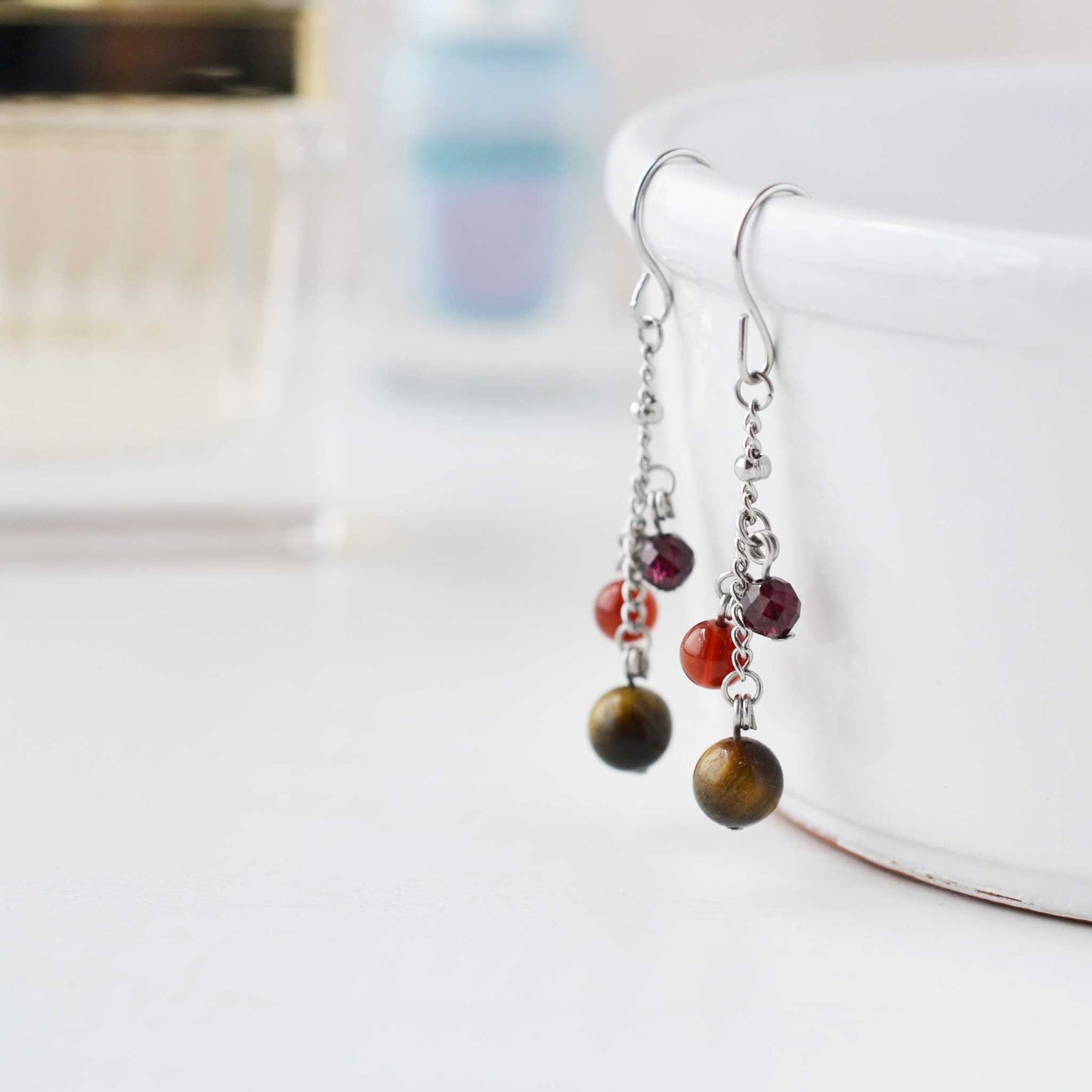 Dark coloured gemstone bead drop earrings hanging on white cup against soft focus background