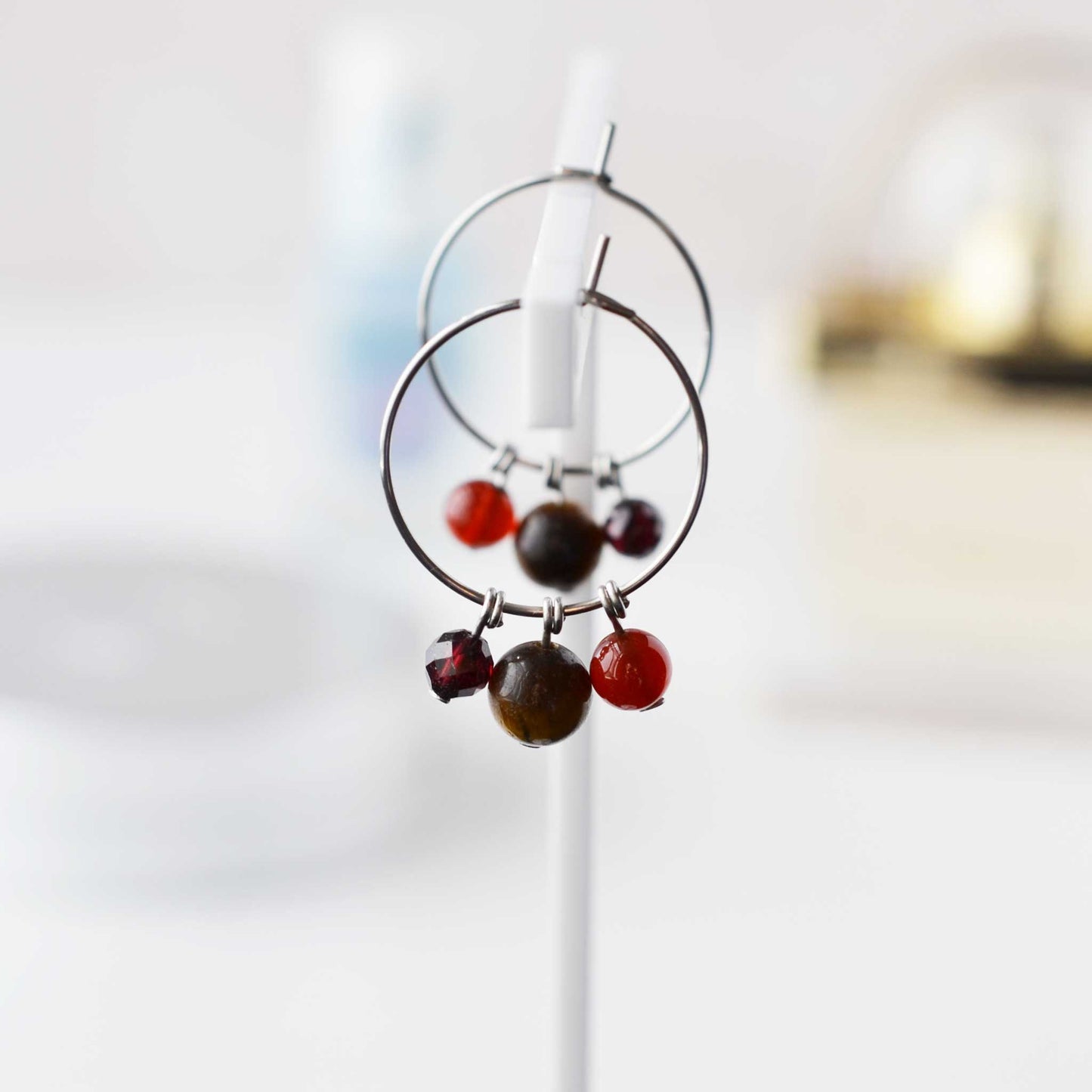 Brown, orange & red gemstone bead hoop earrings hanging against soft focus background