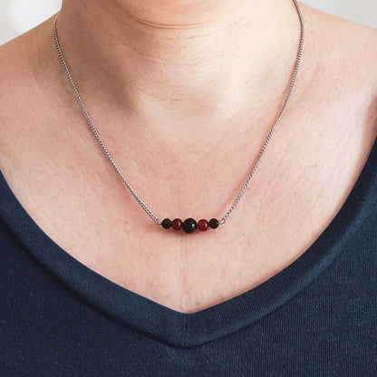 Woman wearing dark blue v neck top and dainty gemstone bead necklace