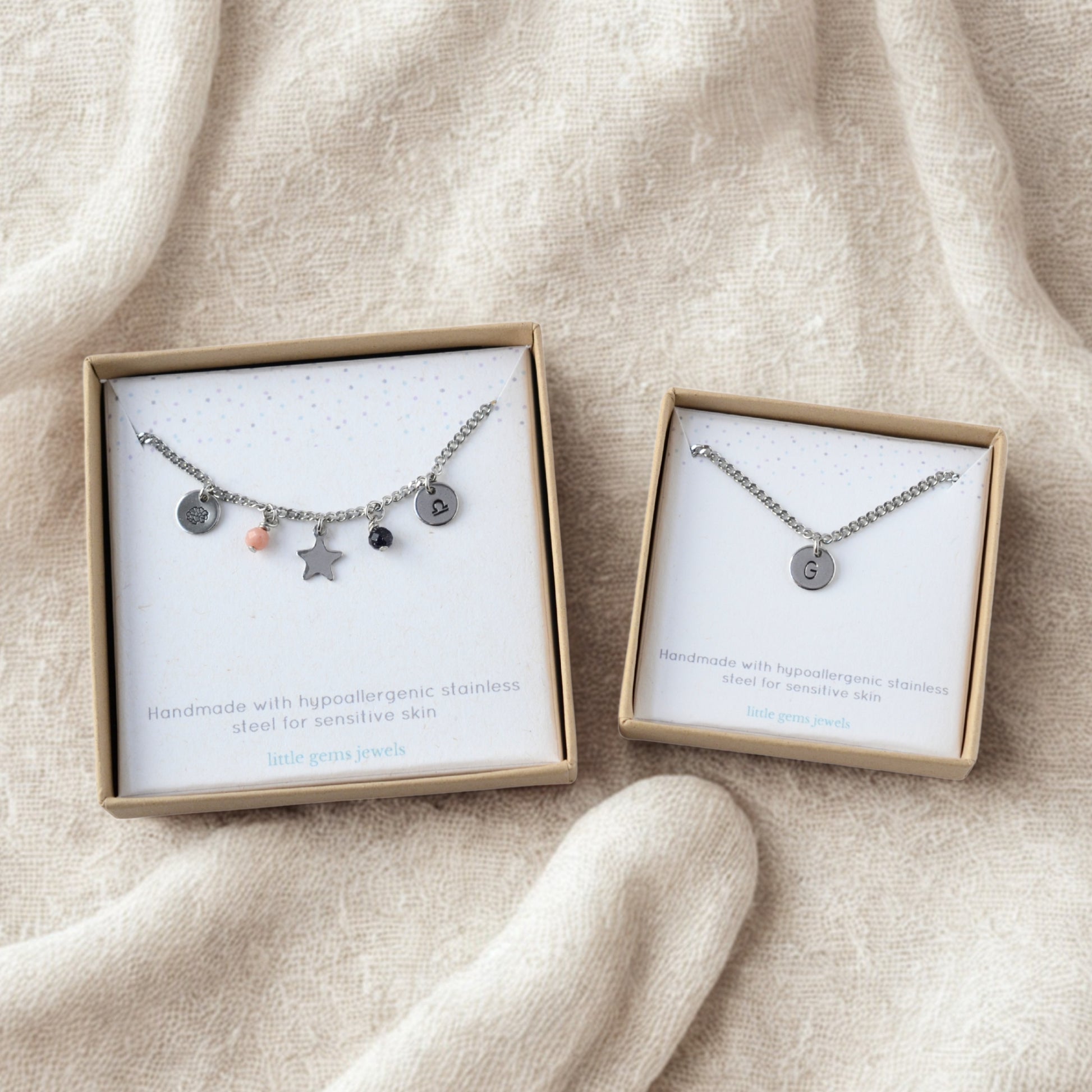Single custom charm necklace and multi custom charm necklace in gift boxes laying on soft neutral fabric.