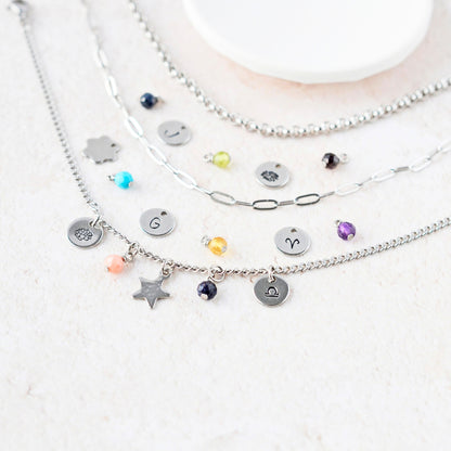 Close up of various tiny gemstone charms and hand stamped steel disc charms next to three different chain styles.
