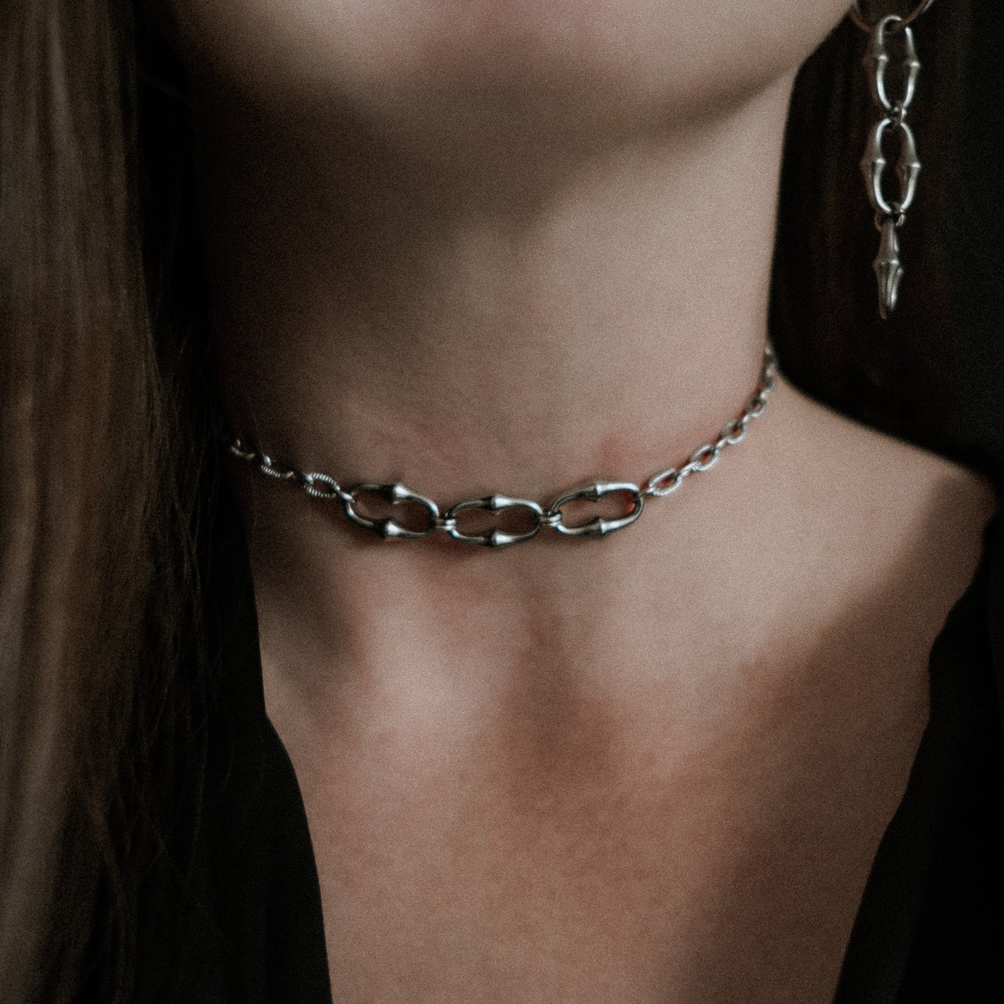 Close-up of a person wearing a steel chain necklace on a dark background