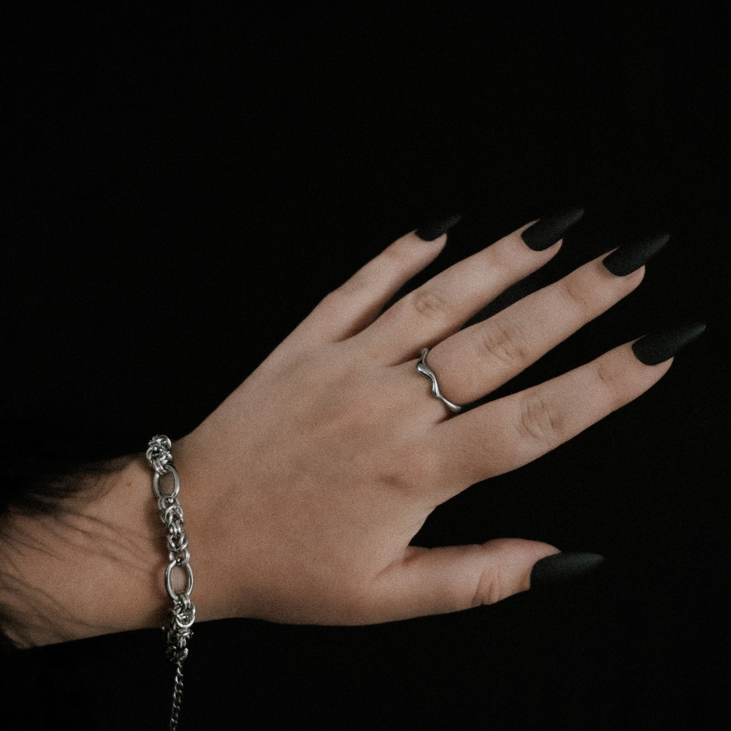 Hand with steel ring and bracelet against a black background