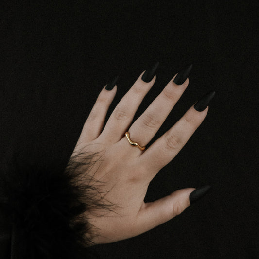Hand with black nail polish wearing a gold ring on a dark background