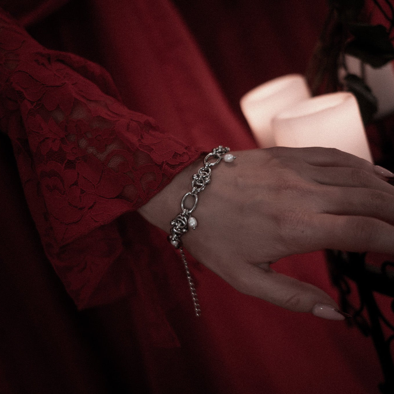 Close-up of a hand wearing a bracelet with a red garment in the background