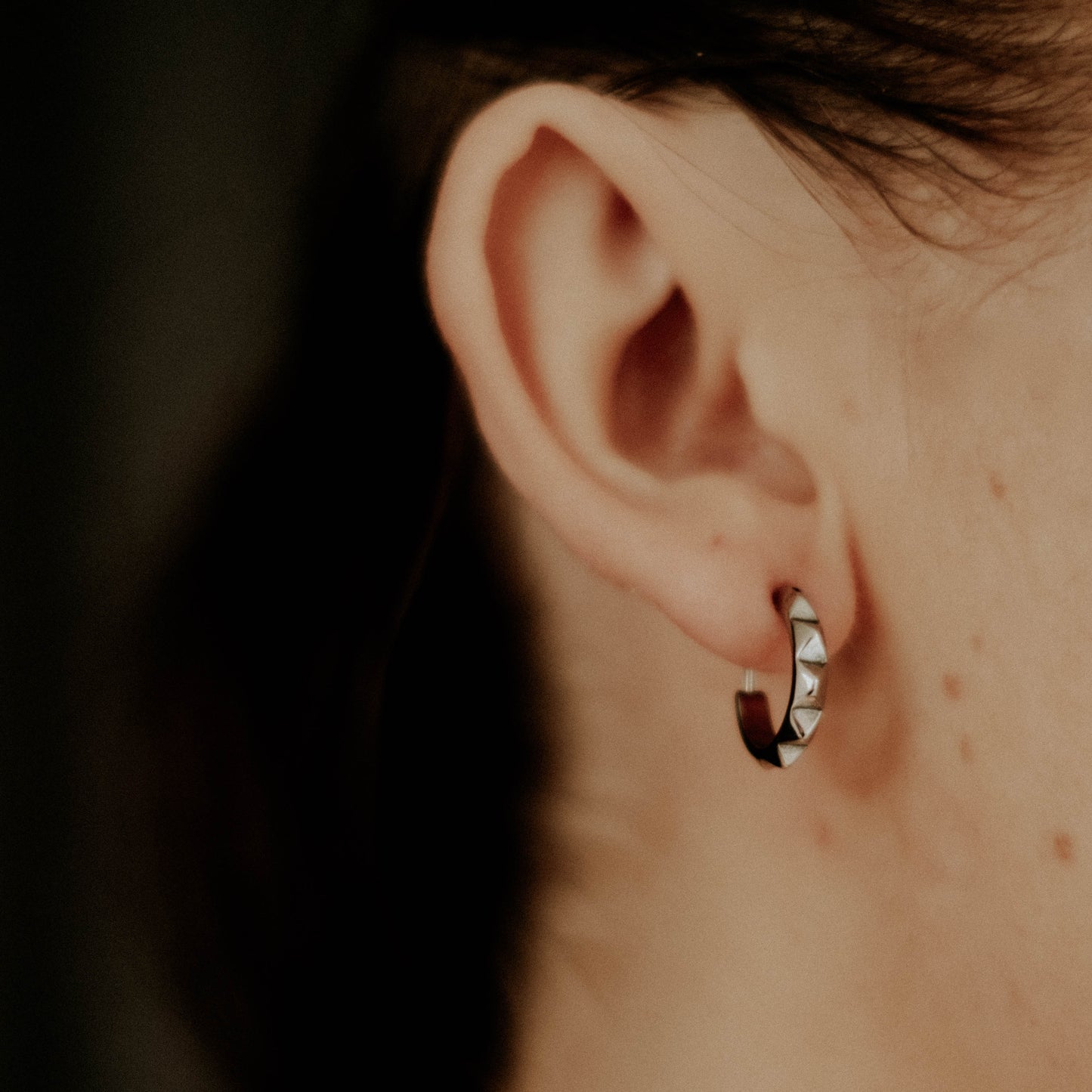 Close-up of an ear wearing a small hoop earring with a dark background