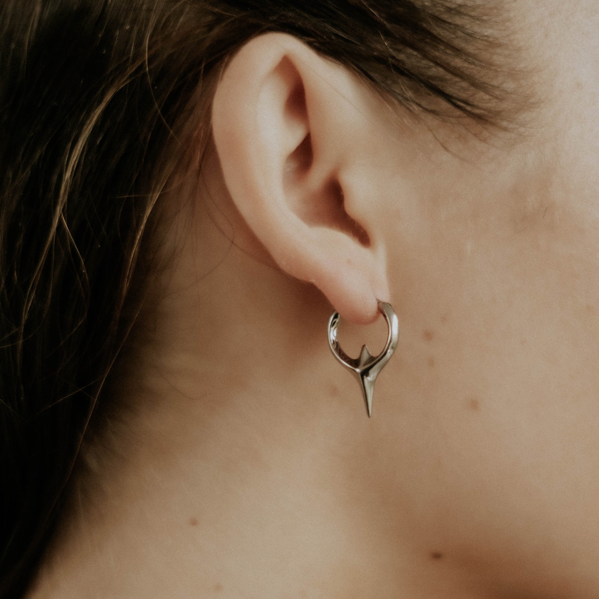 Close-up of an ear wearing a unique steel hoop earring with a blurred background