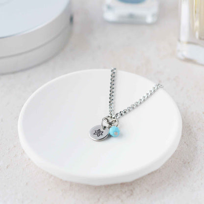 Tiny Poinsettia & Turquoise gemstone necklace laying in white trinket dish