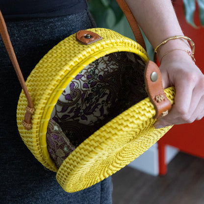 Yellow woven handbag with leather straps held by a person against a blurred background