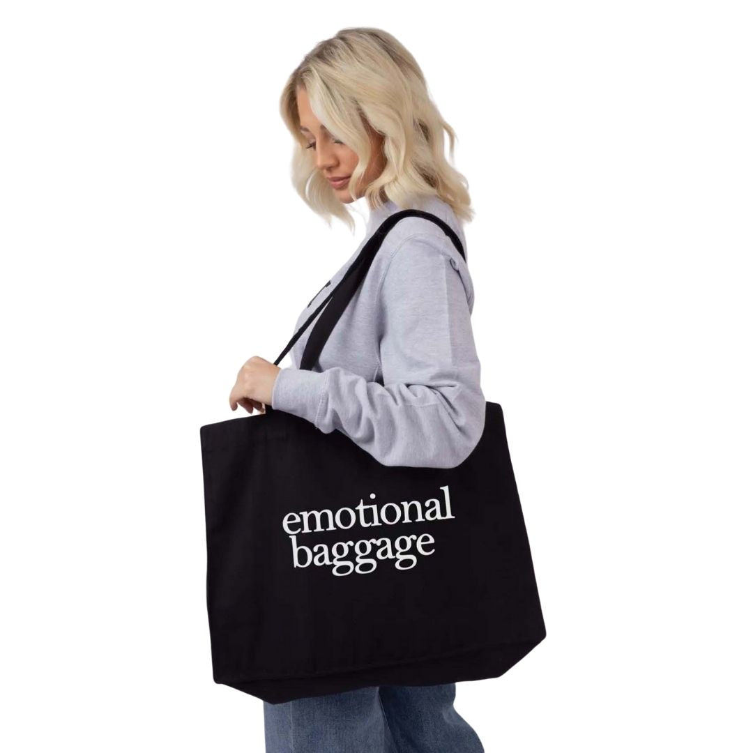 Person holding a black tote bag with 'emotional baggage' text on a white background