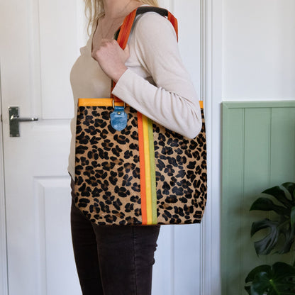 Person holding a leopard print tote bag with orange accents indoors.